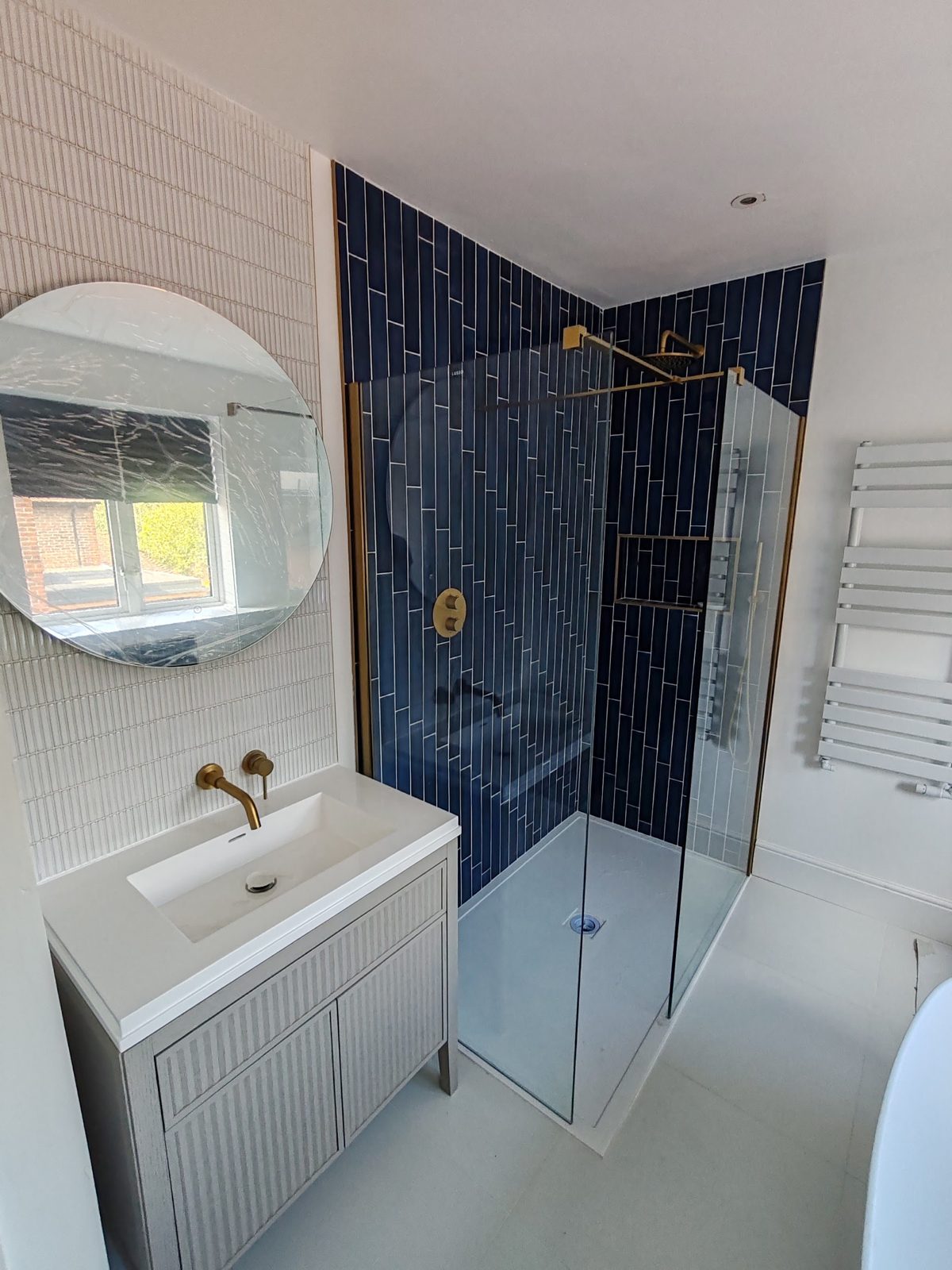 Finished bathroom with a navy tiled shower wall, white tiles and brass fittings