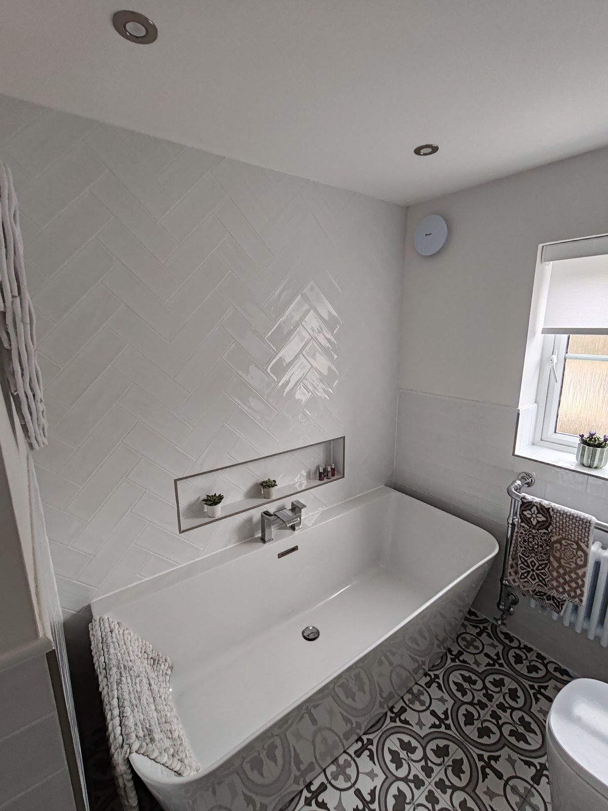 Bathroom with white herringbone wall tiles, a freestanding bath and a patterned floor
